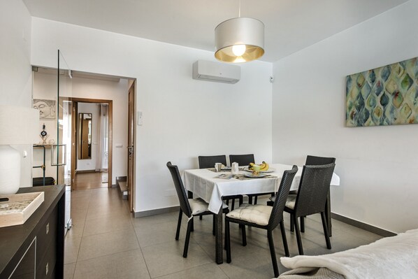 Un comedor moderno con una mesa blanca, cuatro sillas y una lámpara colgante.