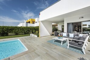 Un espacio al aire libre moderno con piscina, un sofá y una mesa de comedor.