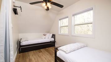 A bedroom with two single beds, a ceiling fan, and two windows.