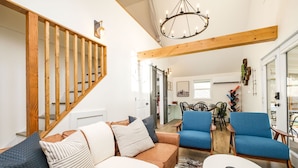 A spacious living room with a wooden staircase, a chandelier, a sofa set, and a dining area with blue chairs. - Private, Hot tub, Firepit, Bocce Ball, Horse Shoes, Outdoor Ping Pong Table (Shenandoah)