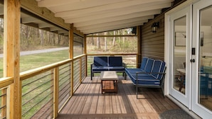 A covered deck with wooden railings, a blue sofa, and a small table. - Private, Hot tub, Firepit, Bocce Ball, Horse Shoes, Outdoor Ping Pong Table (Shenandoah)