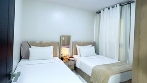 Une chambre d’hôtel avec deux lits, une table de chevet avec une lampe, un miroir et une fenêtre avec des rideaux.