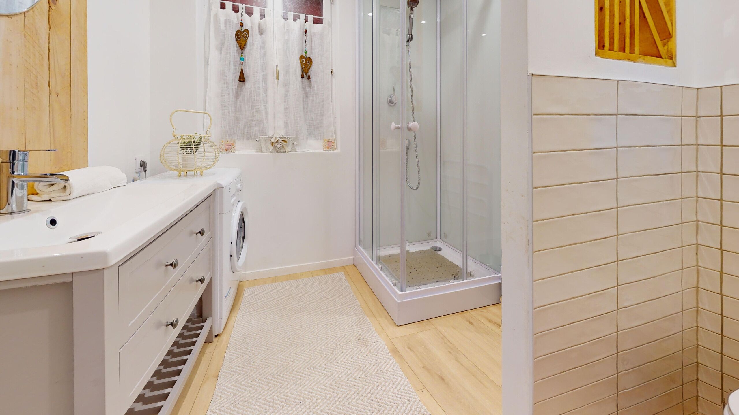 A bathroom with a white sink, a washing machine, a glass shower enclosure, and a tiled wall.