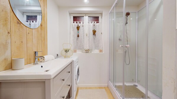 A modern bathroom with a wooden vanity, a glass shower enclosure, and a window with decorative curtains.