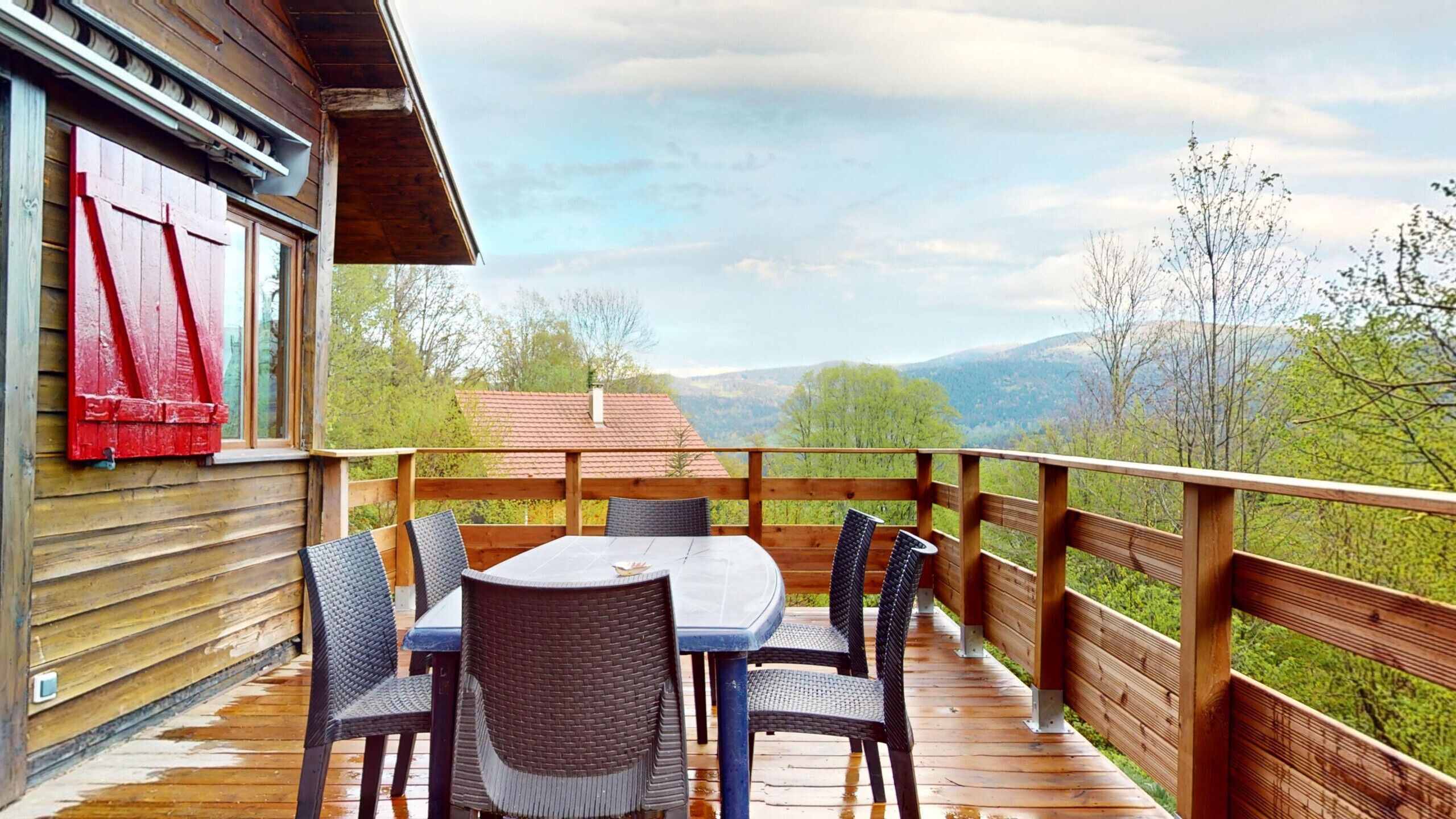 A wooden deck with a table and chairs, overlooking a mountainous landscape.