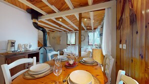 Un coin repas avec une table en bois dressée pour quatre personnes, des chaises blanches et une cuisine visible au fond.