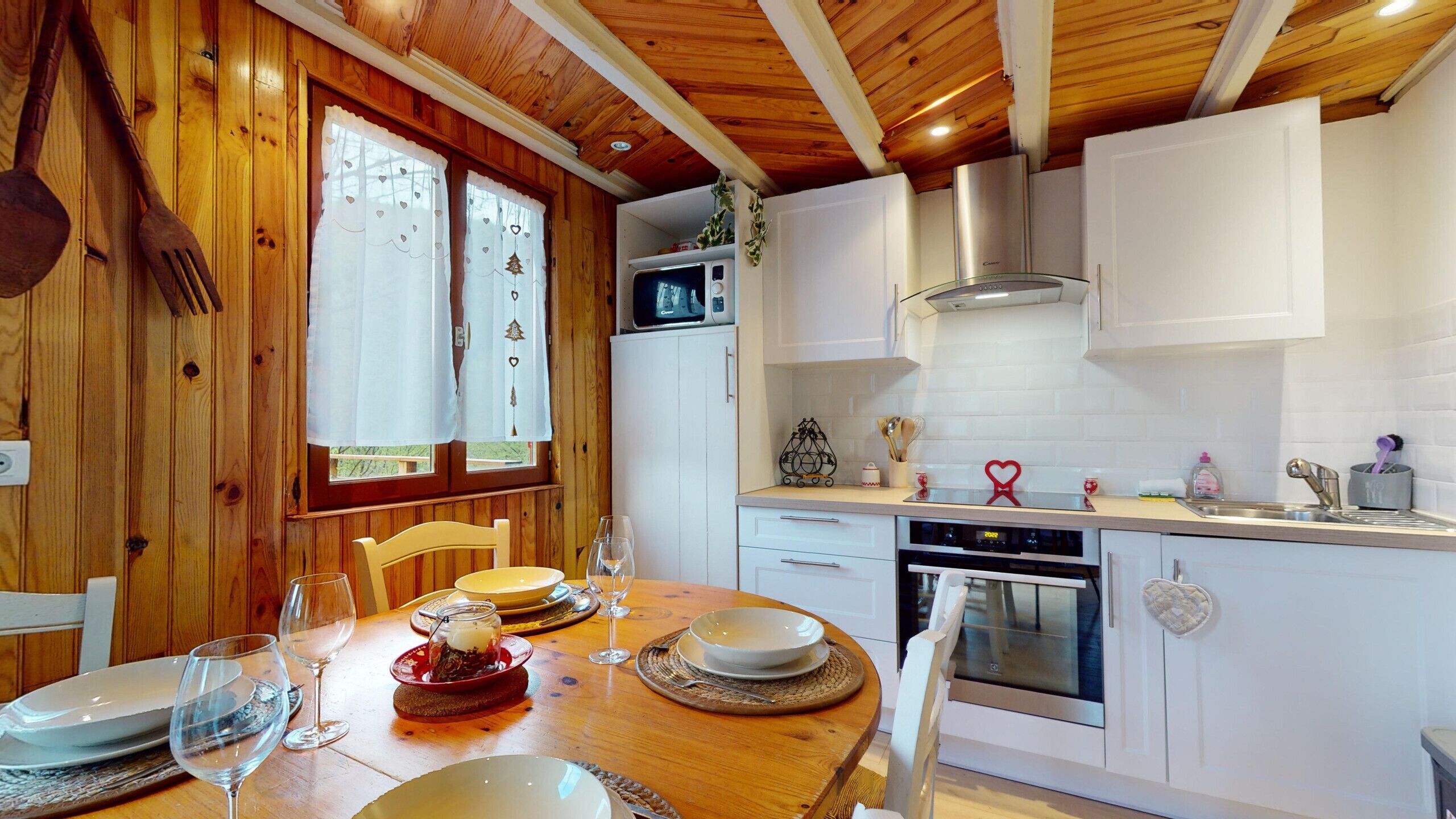 A wooden interior with a dining table set for two, a microwave, oven, and white cabinets.