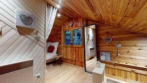 Une chambre confortable dans un chalet, avec des murs en bois, un lit recouvert de draps blancs, une petite table et une fenêtre donnant sur les arbres.