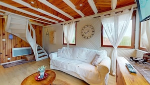 Une pièce chaleureuse avec un canapé blanc, des poutres en bois au plafond, une horloge et un escalier.