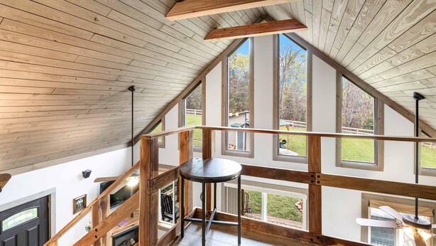 Une chambre spacieuse aménagée en mezzanine, avec un plafond haut, de grandes fenêtres et un escalier en bois.