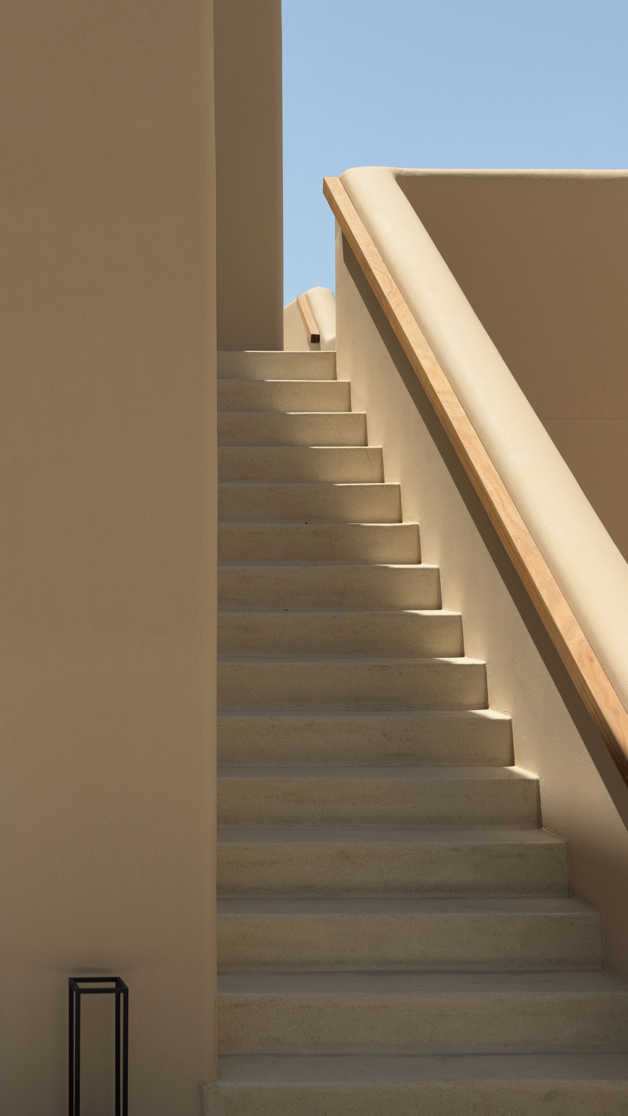A staircase with a wooden handrail and beige walls.