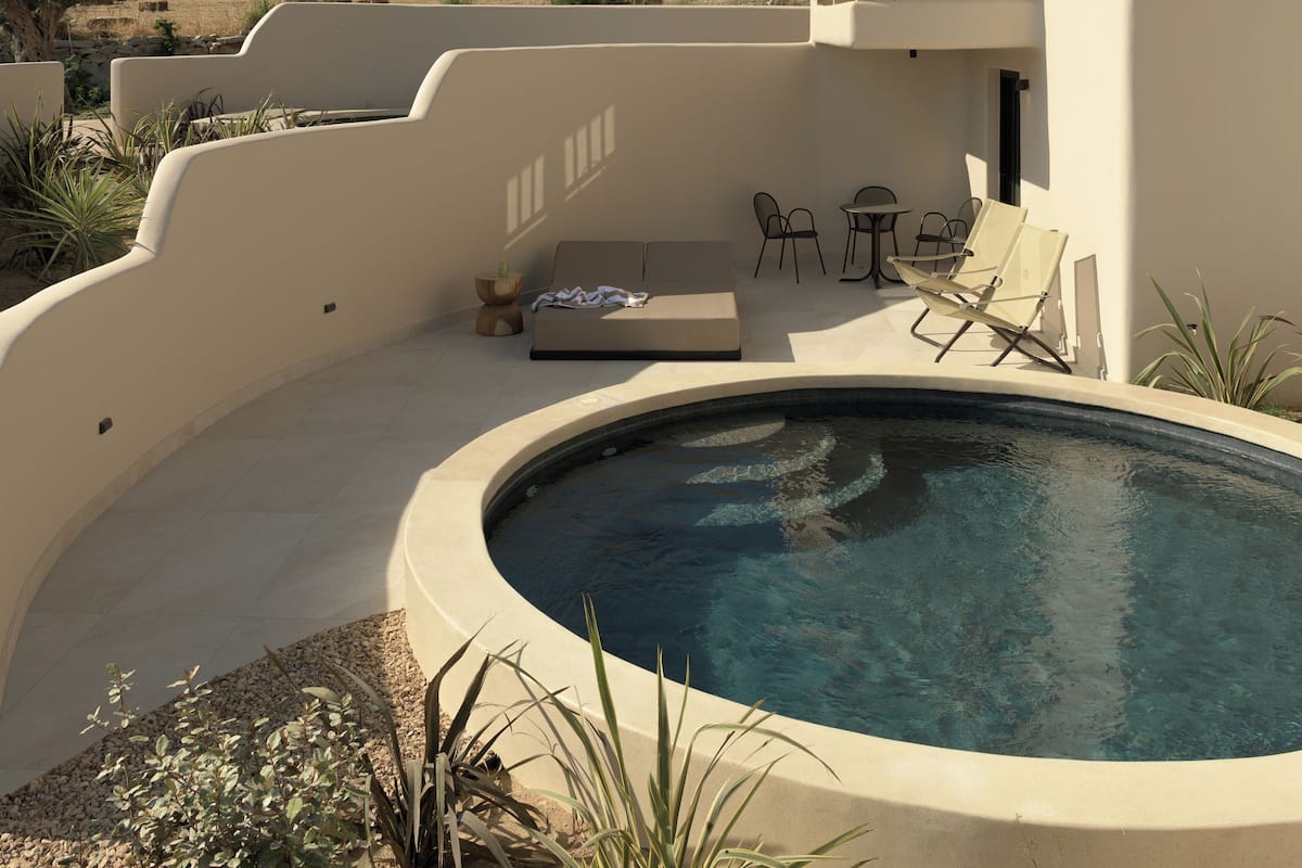 A modern outdoor pool area with a curved pool, lounge chairs, and a seating area with a sofa and chairs.