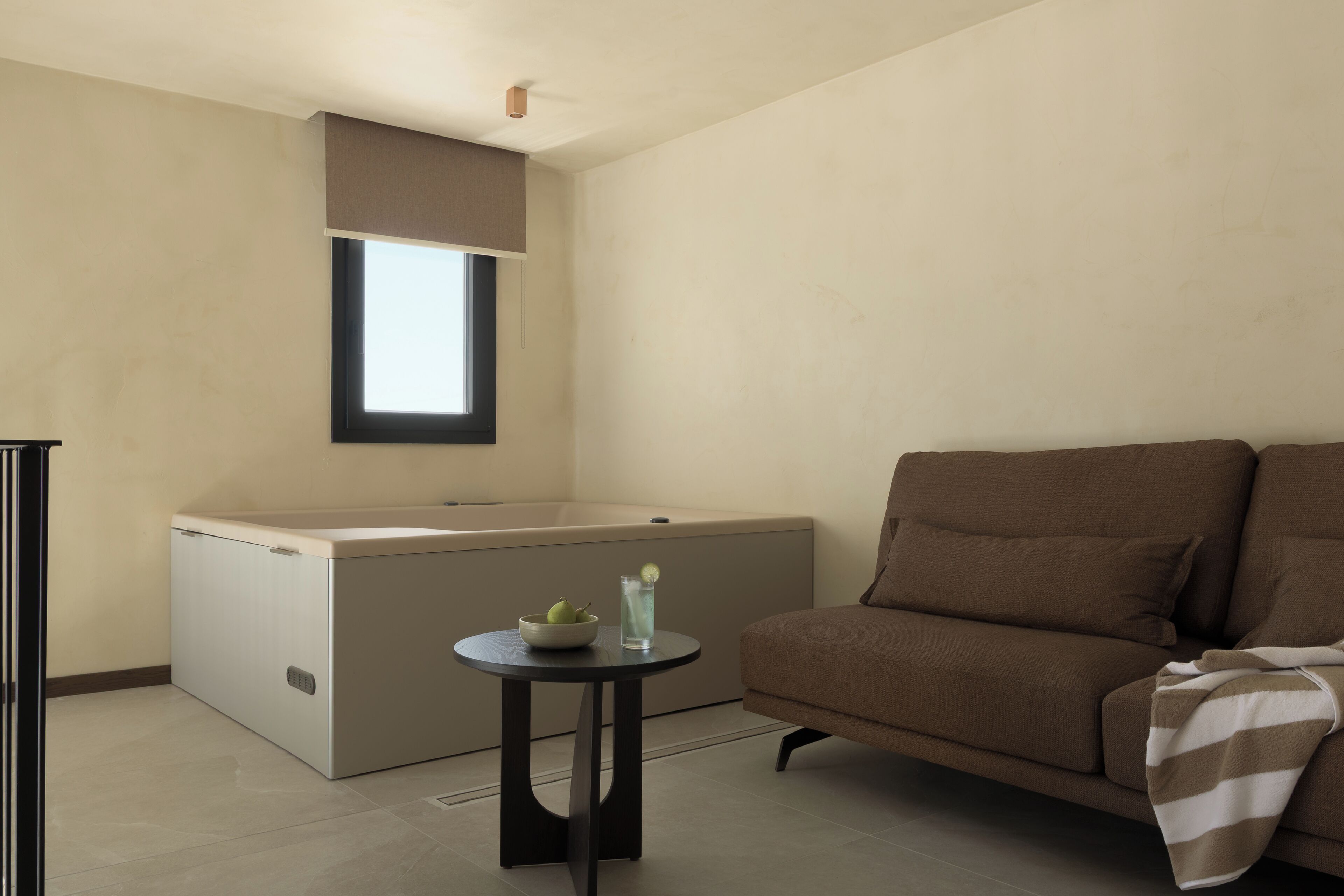 Un salon moderne avec un canapé, une petite table ronde sur laquelle se trouvent un bol et un verre, et une baignoire intégrée.