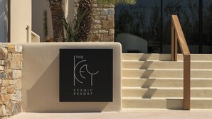 A sign for The Scenic Resort with a minimalist design, a stone wall, and a wooden staircase. - The Key  (Naxos)