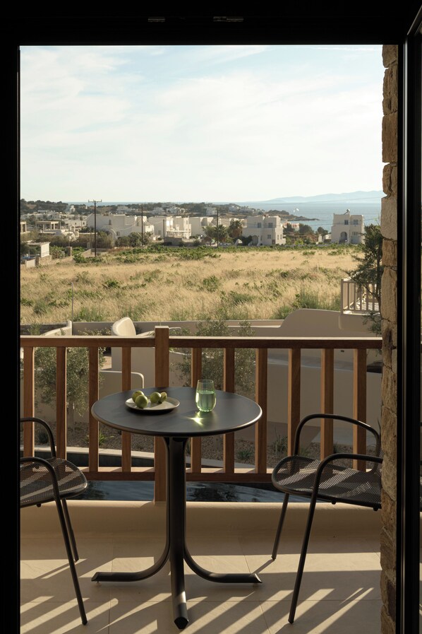 A balcony with a table and chairs, overlooking a beach and distant buildings. - The Key (Naxos)