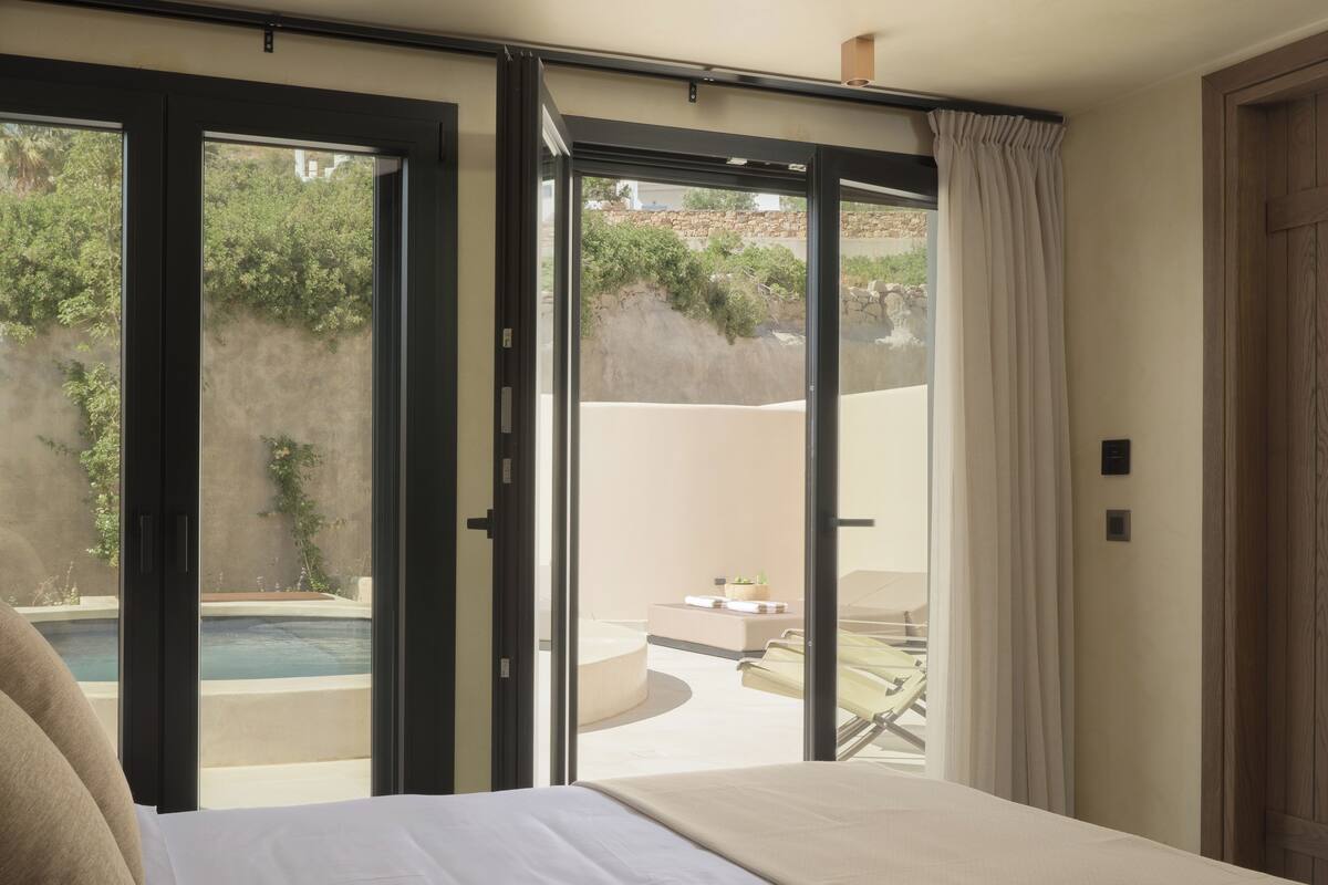 A bedroom with a bed, a sliding glass door leading to an outdoor area with a pool and lounge chairs.