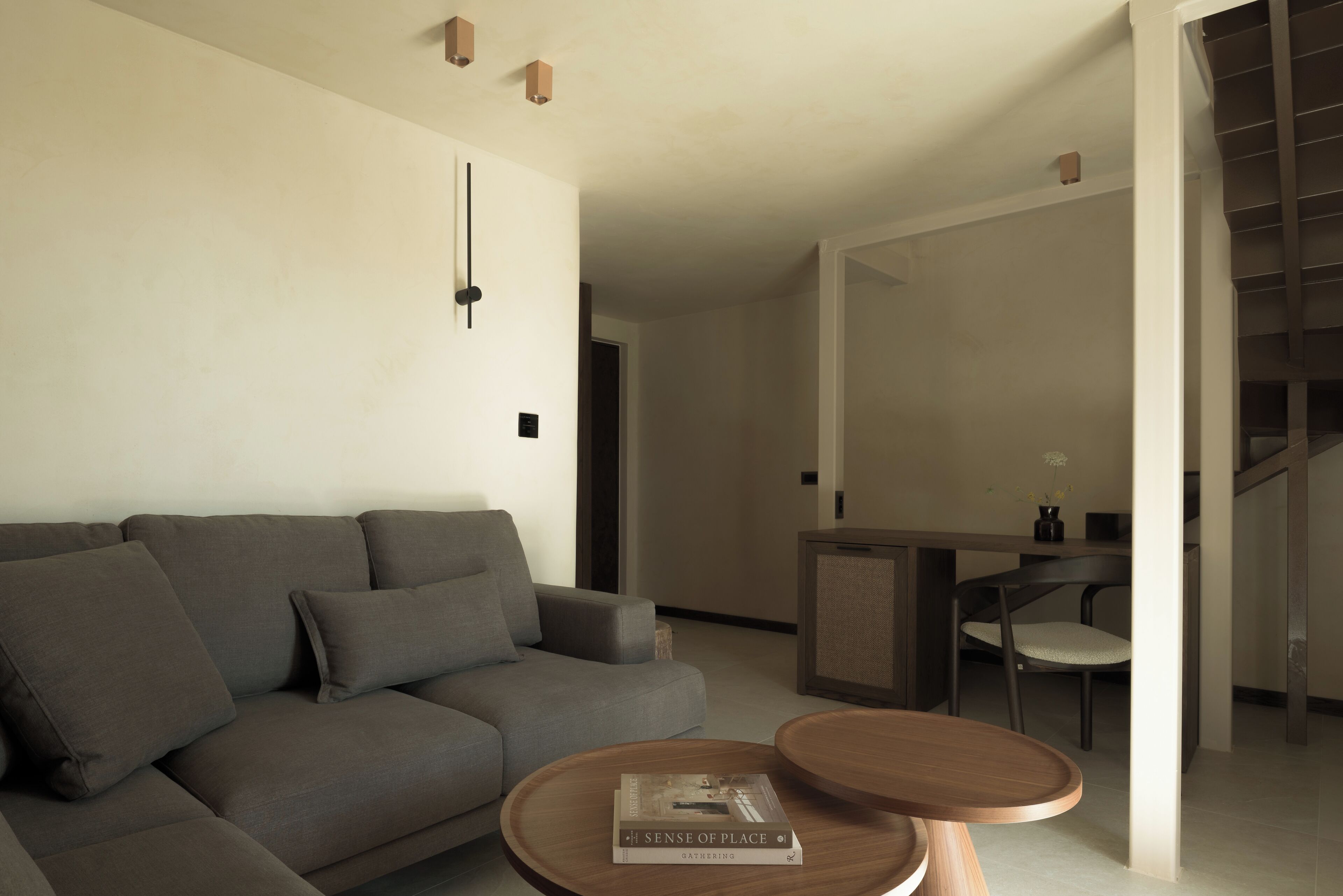 A modern living room with a grey sofa, two wooden side tables, and a book titled "Sense of Place" on one of the tables.