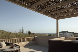 Terraza en la azotea con un sofá curvo, baranda de madera y vista al mar y edificios lejanos.