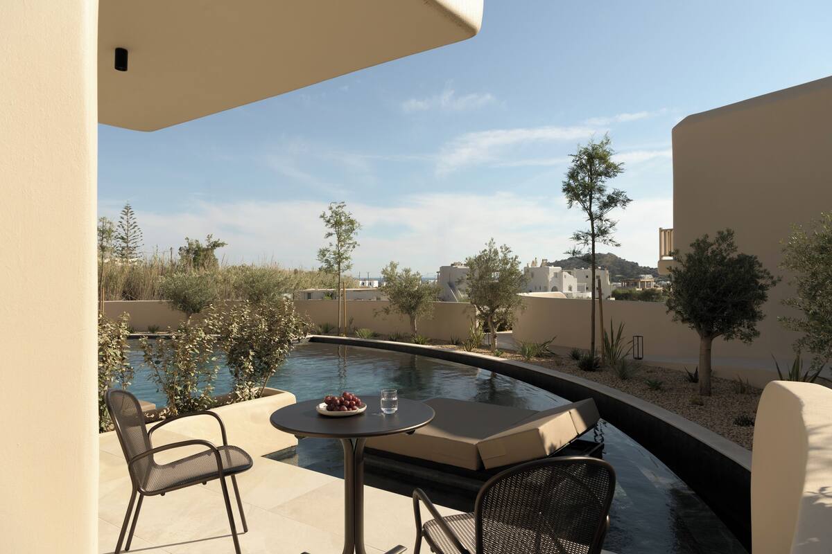A poolside area with a table and chairs, a bowl of fruit, and a glass of water.