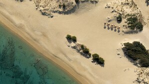 An aerial view of a beach with clear turquoise water, sandy shore, and scattered vegetation. - The Key  (Naxos)