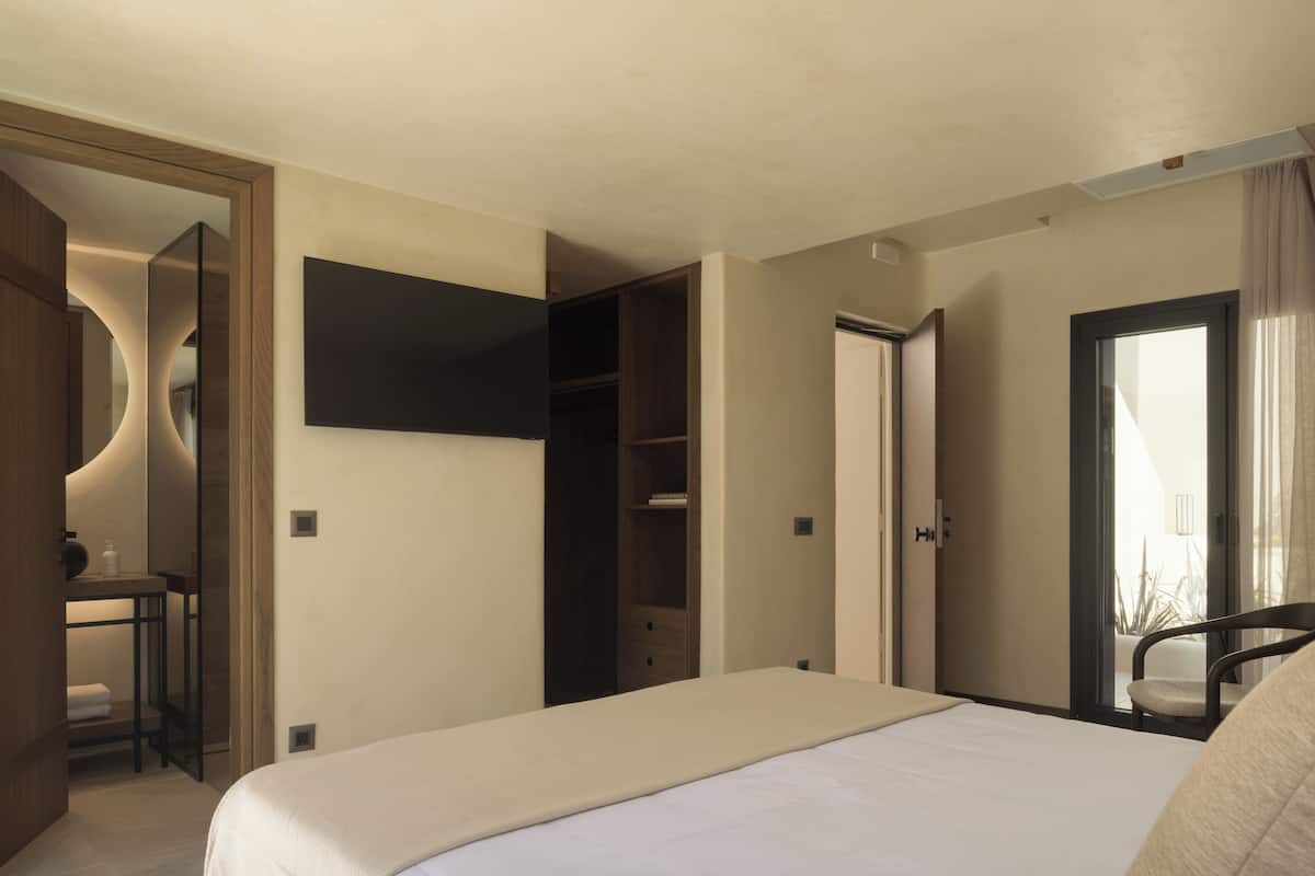 A hotel room with a bed, a desk, a wardrobe, and a TV mounted on the wall.