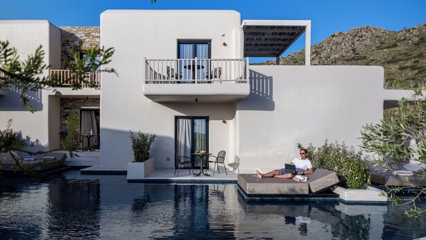 A modern building with a pool, a balcony with outdoor furniture, and a person relaxing by the pool. - The Key  (Naxos)