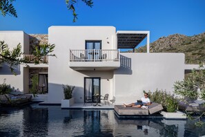 A modern building with a pool, a balcony with outdoor furniture, and a person relaxing by the pool. - The Key (Naxos)