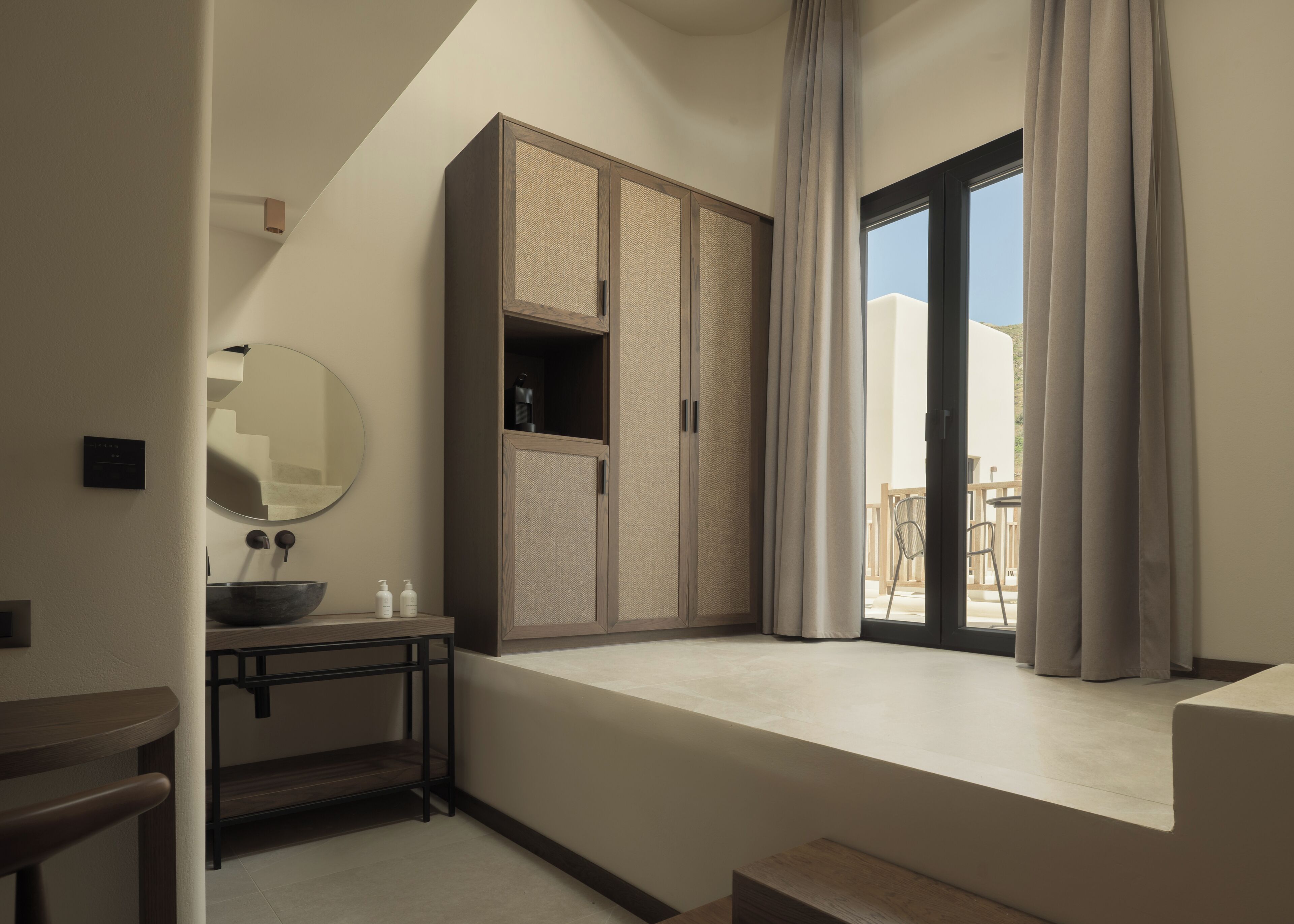 Une salle de bain moderne avec un grand meuble de rangement, un lavabo sur colonne, un miroir et une fenêtre avec des rideaux.