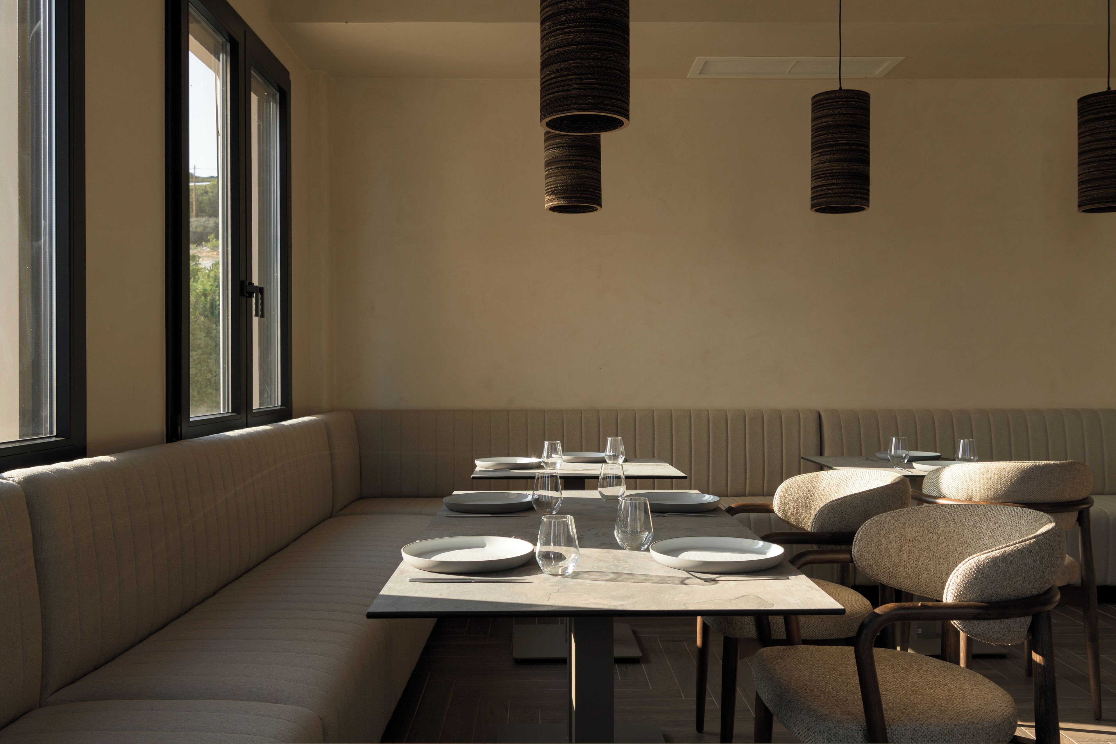 Un espace repas comprenant un long banc, des tables et des chaises, ainsi que des luminaires suspendus.