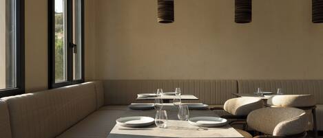 Un espace repas comprenant un long banc, des tables et des chaises, ainsi que des luminaires suspendus.