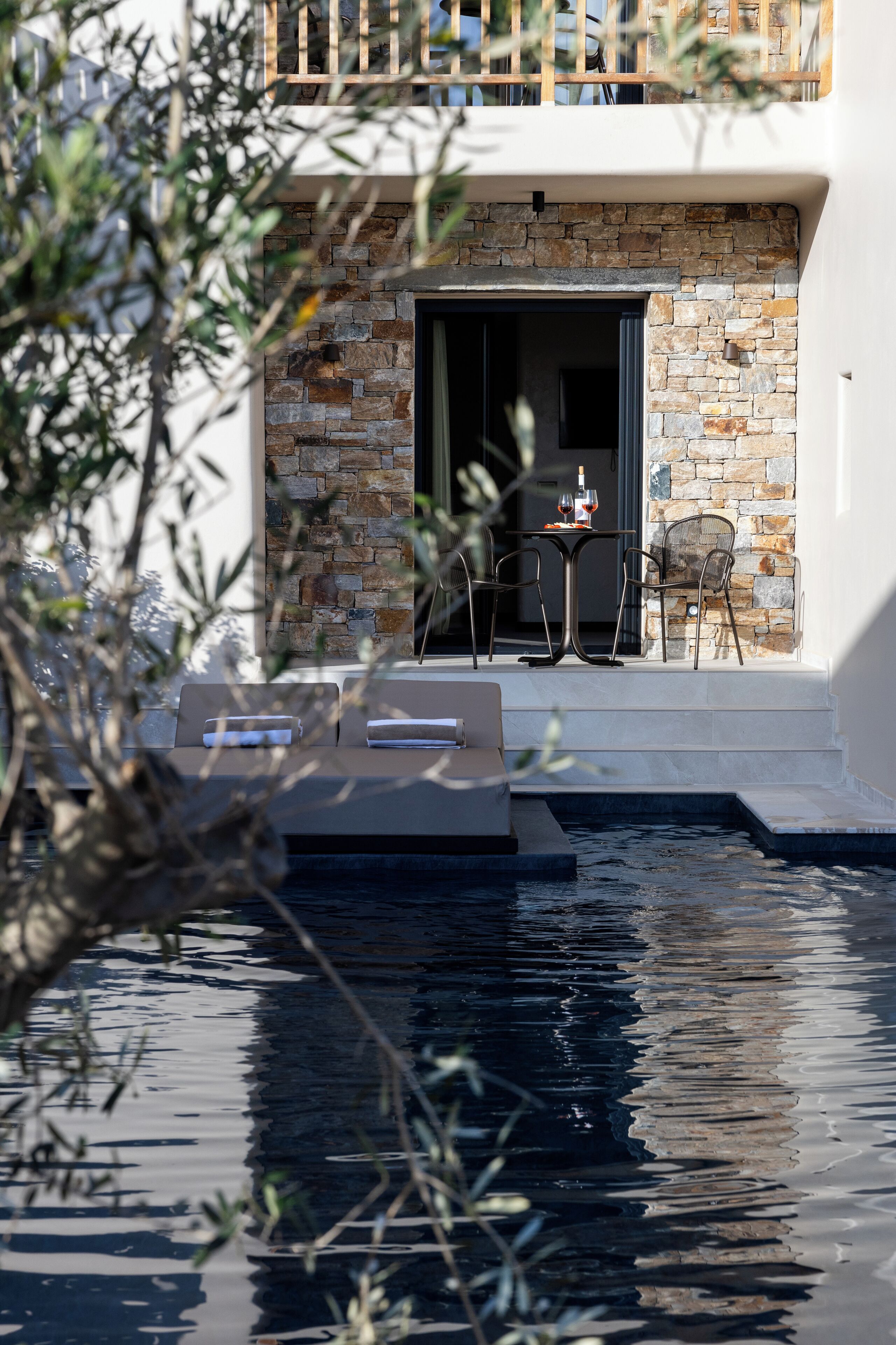 Un espace extérieur moderne, aménagé avec un mur en pierre, une piscine et une table entourée de chaises.