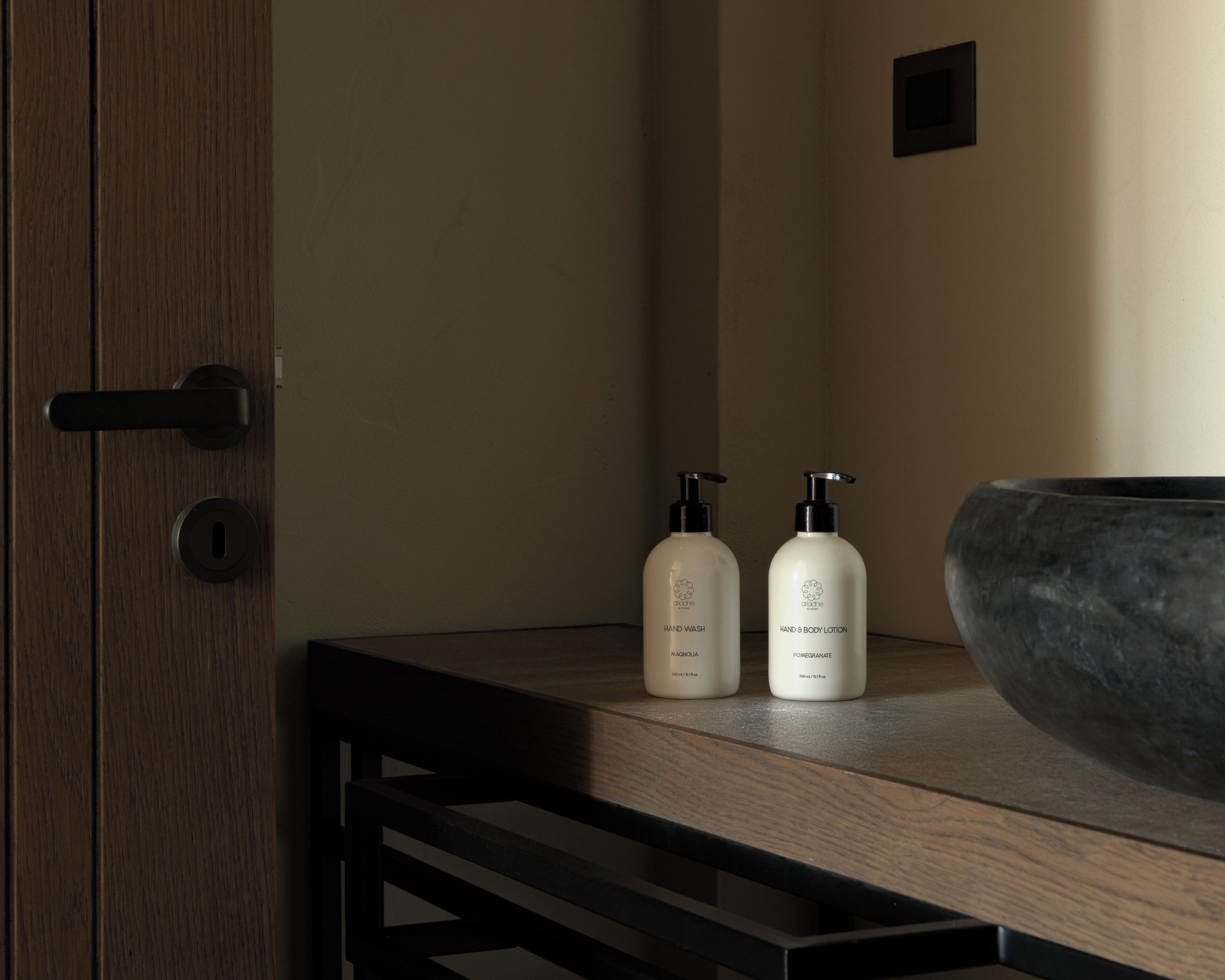 Un baño con tocador de madera, dos botellas dispensadoras de jabón para manos y un lavabo de piedra grande.