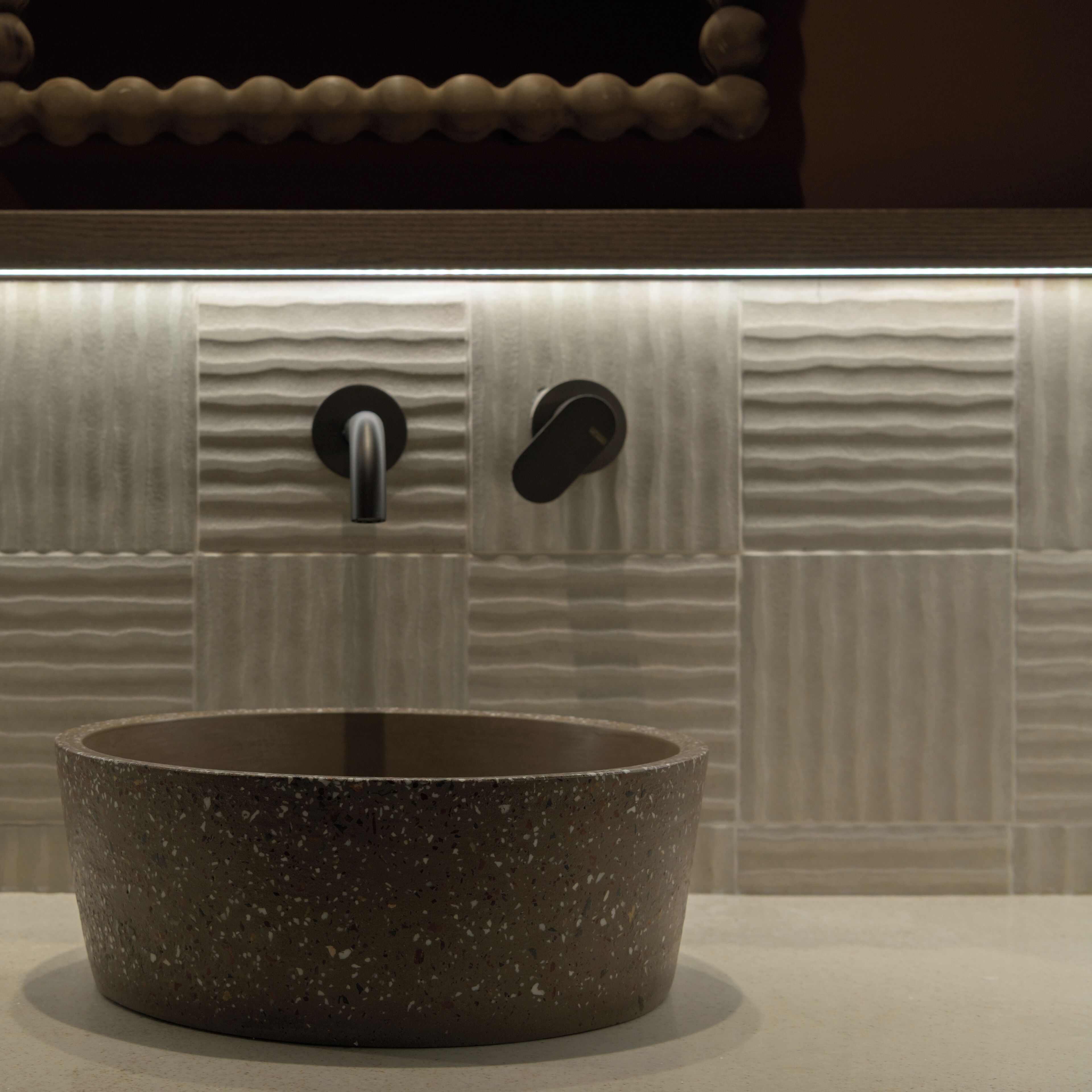 Un bagno con un lavandino in ceramica effetto venato, un rubinetto moderno e una parete strutturata con modanatura decorativa nella parte superiore.