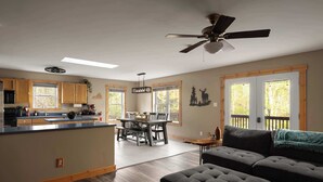 A spacious living area with a dark gray sofa, a dining table with chairs, and a kitchen area with wooden cabinets and a countertop. - The Haven at Turkey Run • Hot Tub, Fire Pit, Games (Strasburg)