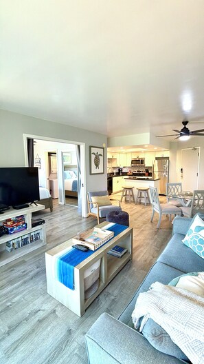 A spacious living room with a sofa, coffee table, and TV, leading to a kitchen with modern appliances.