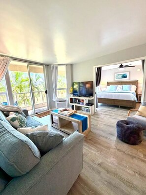 A hotel room with a sofa, a TV, a bed, and a balcony with curtains.