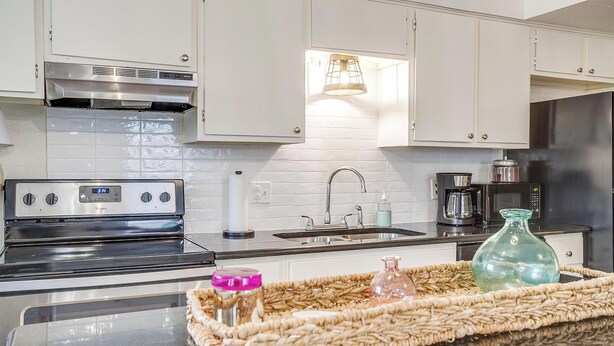 A modern kitchen with white cabinets, stainless steel appliances, a digital clock, and a woven tray with jars. - The Verde in the Fort! (Fort Worth)