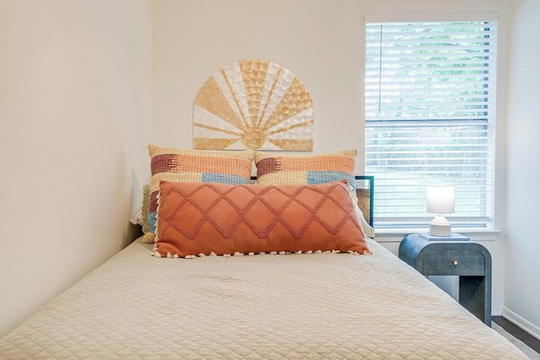 A bed with a quilted headboard, a decorative wall piece, and a bedside table with a lamp. - The Verde in the Fort! (Fort Worth)
