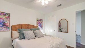 A bedroom with a large bed, a wooden headboard, two wall-mounted paintings, a mirror, and a door leading to another room. - The Verde in the Fort! (Fort Worth)