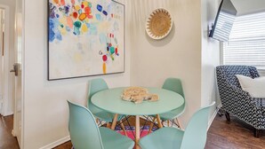 A dining area with a round table and four chairs, a large abstract painting, a woven wall art piece, and a patterned armchair. - The Verde in the Fort! (Fort Worth)