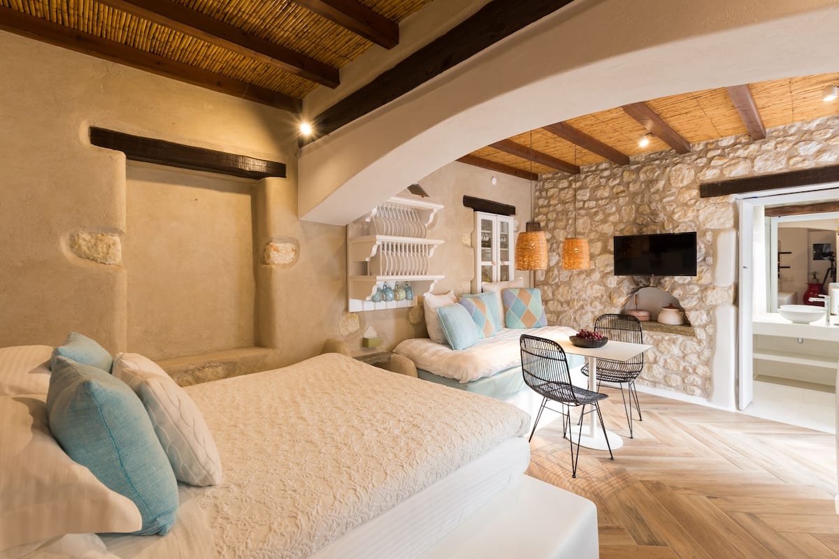 A bedroom with a bed, a desk, and a stone wall.