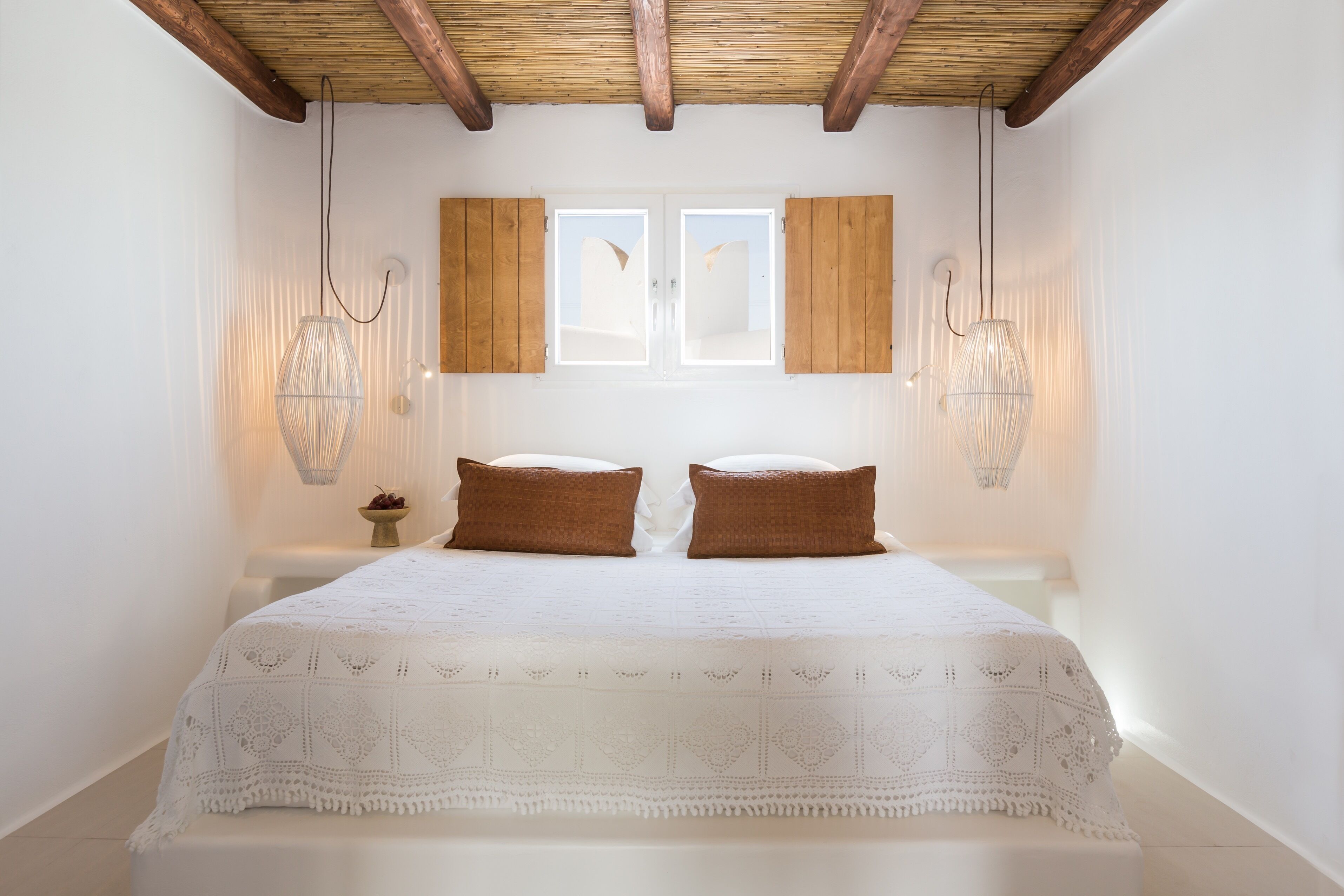 Une chambre avec un grand lit, deux fenêtres, des poutres en bois et des lampes suspendues.