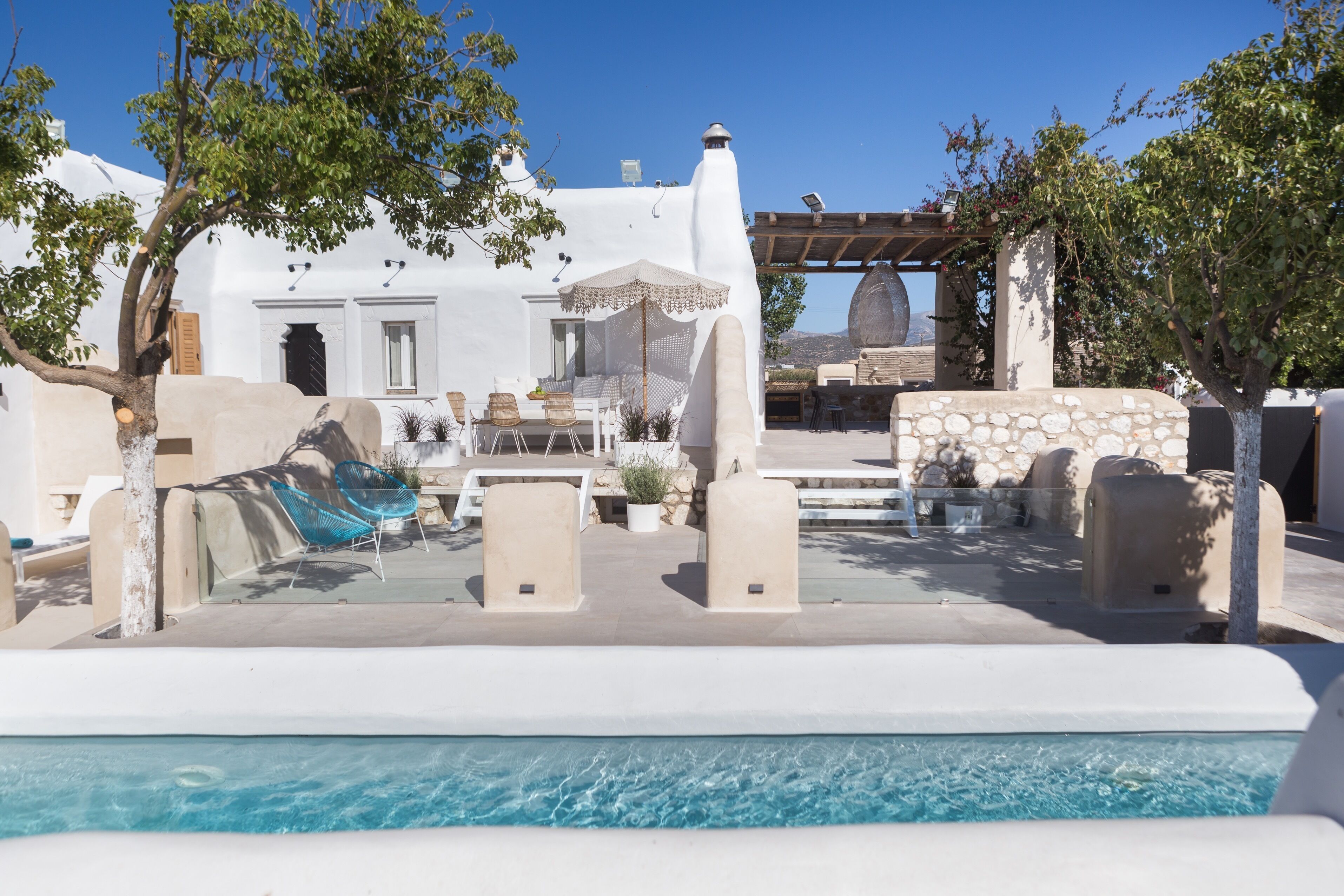 Un espace piscine aménagé avec des chaises longues, une pergola et un mur en pierre.