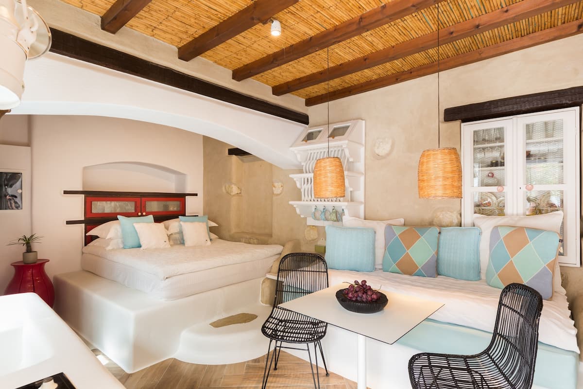 A modern bedroom with a bed, a sofa, two chairs, a small table, and a decorative shelf.