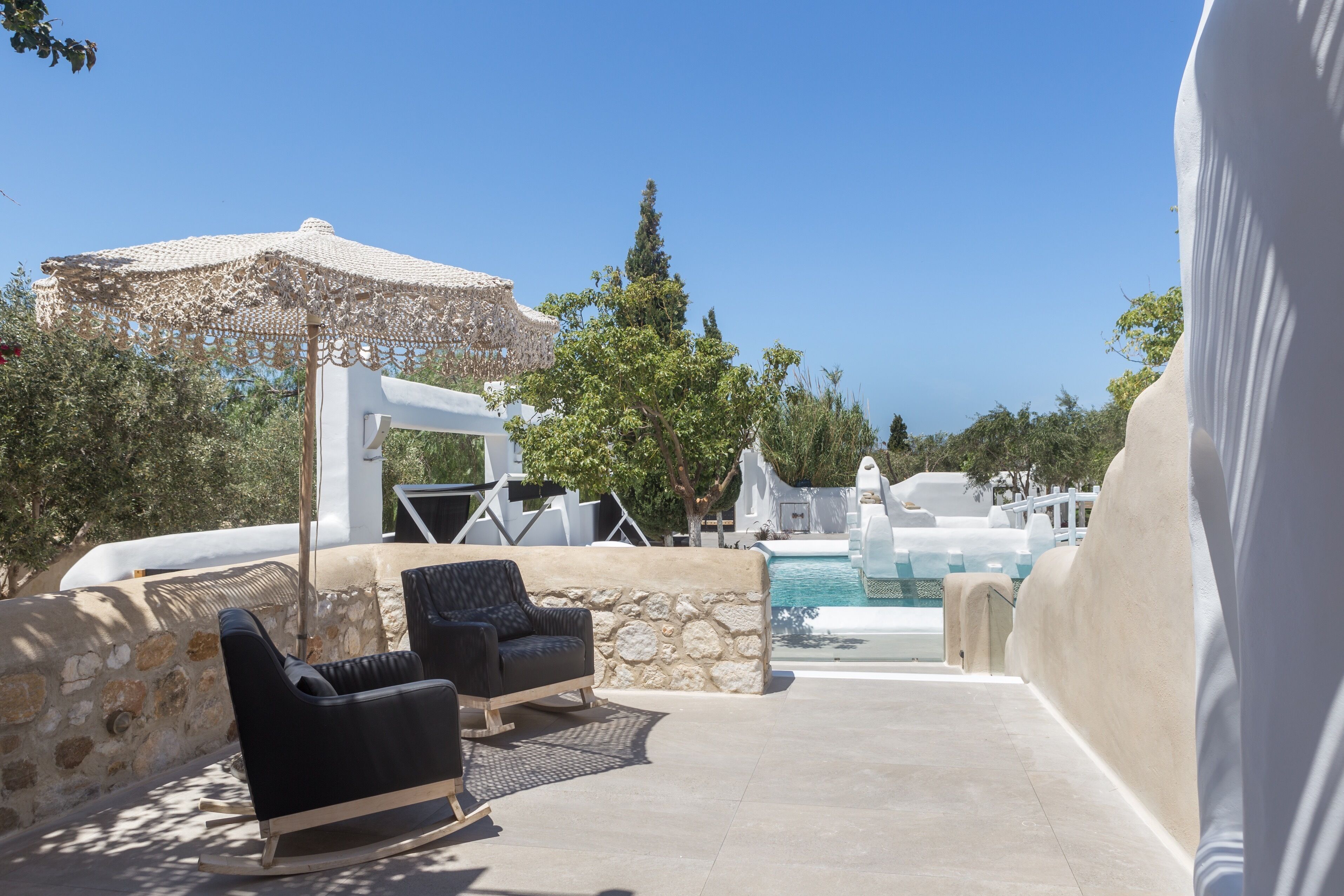 A poolside area with a white umbrella, black lounge chairs, and a stone wall.