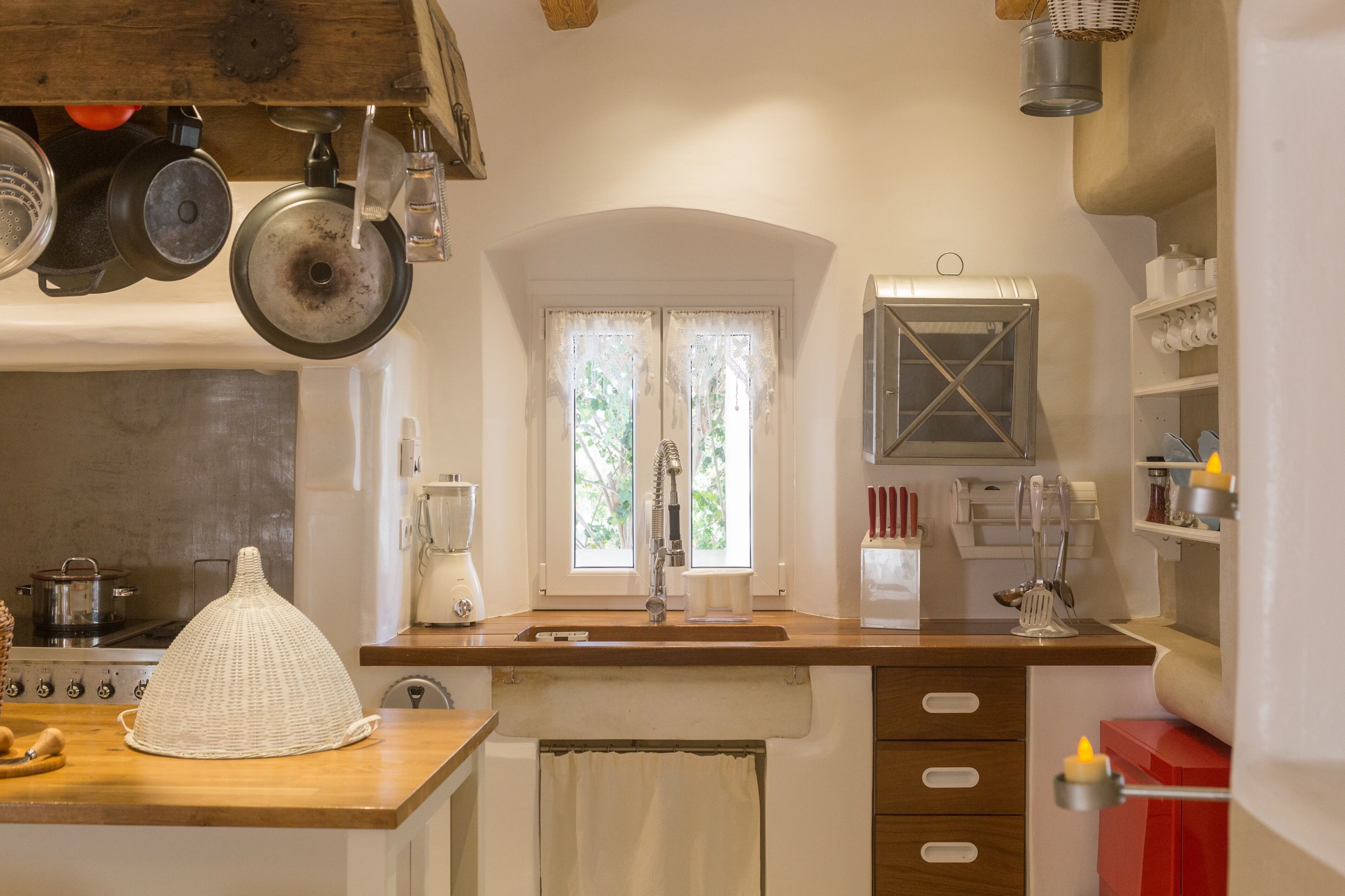 Una cocina con mostrador de madera, un lavamanos, una ventana con cortinas y diversos electrodomésticos.
