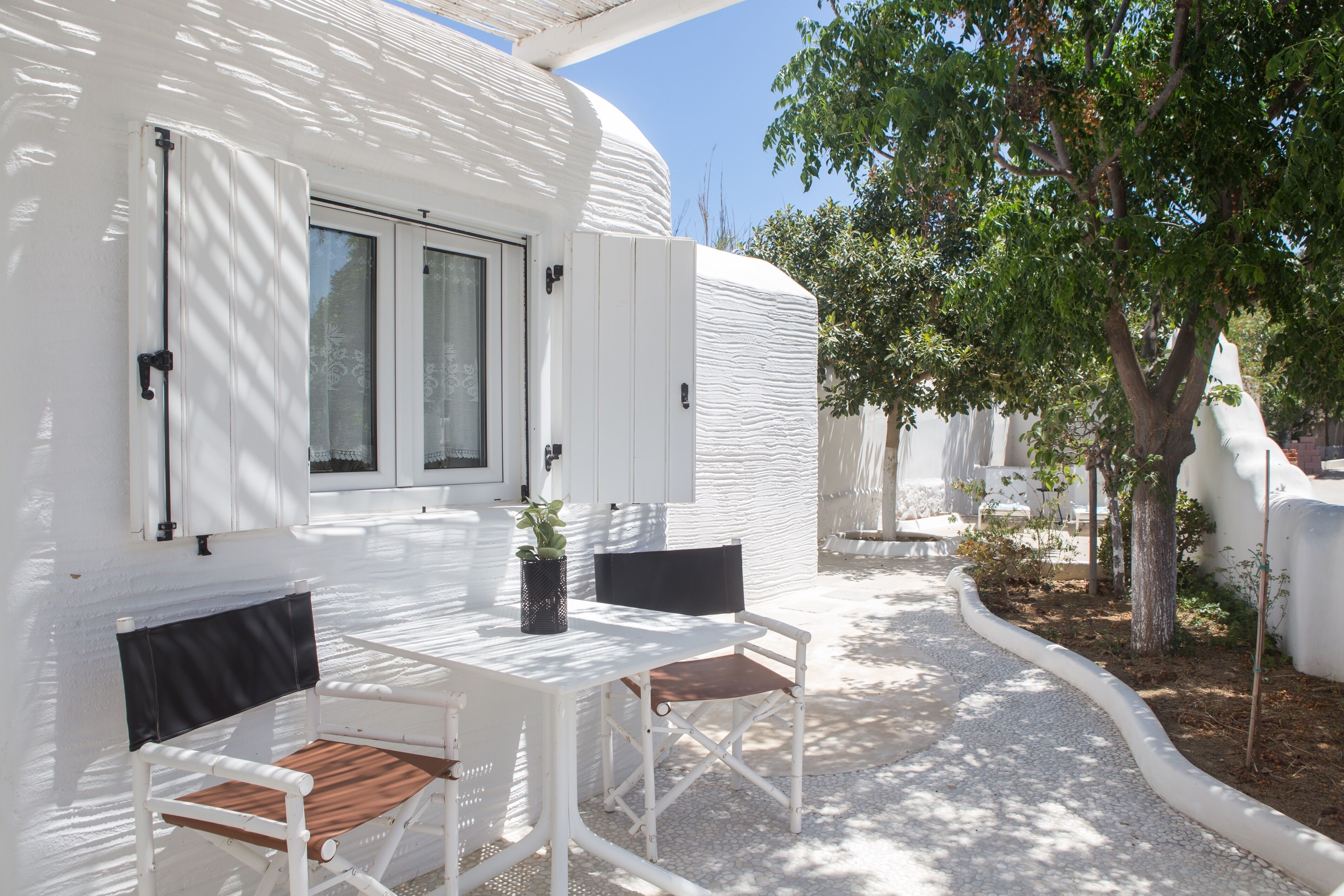 Villa blanca con un patio que cuenta con una mesa, dos sillas, una planta en maceta y vistas del jardín circundante.