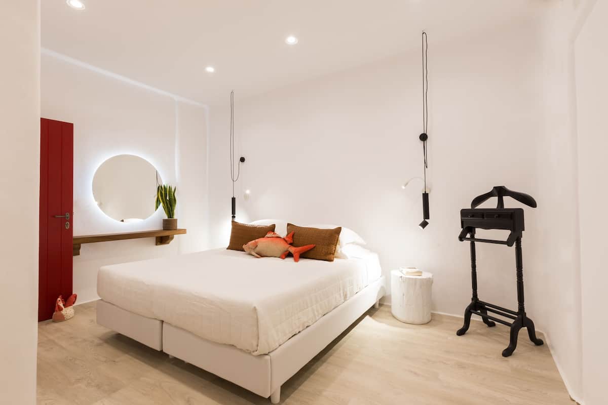 A modern bedroom with a bed, a bedside table, a hanging light fixture, and a red door.