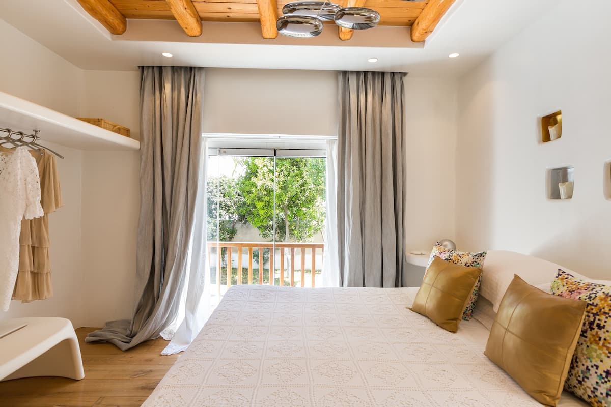 A bedroom with a large bed, a balcony, and a view of greenery outside.