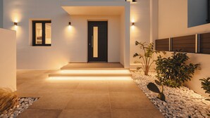 Une maison moderne avec une porte noire, des luminaires fixés aux murs et un chemin menant à l’entrée.